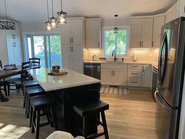 Open-concept kitchen with black island, bar stools, seeded glass pendants and white cabinets facing the dining area