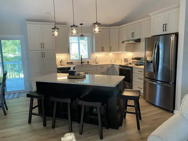 White kitchen remodel with a black island and bar stools, lantern pendants, quartz counters and a stainless refrigerator