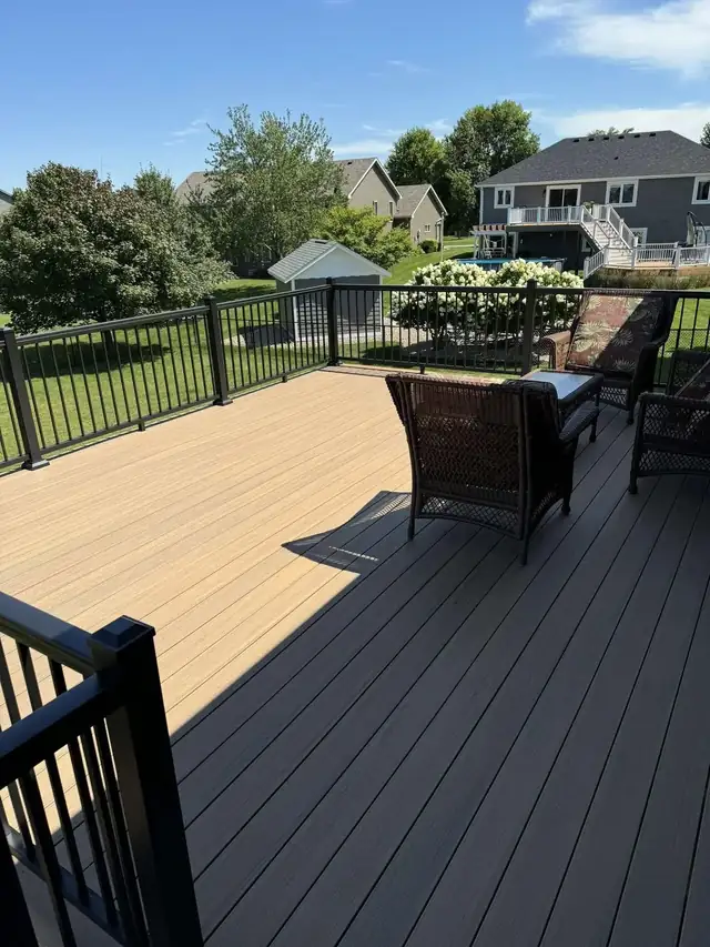 New composite deck with two-tone boards and black metal railing overlooking a backyard