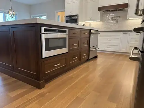Remodeled kitchen with dark stained wood island, built-in microwave drawer, white cabinets, wood range hood and wide-plank floor