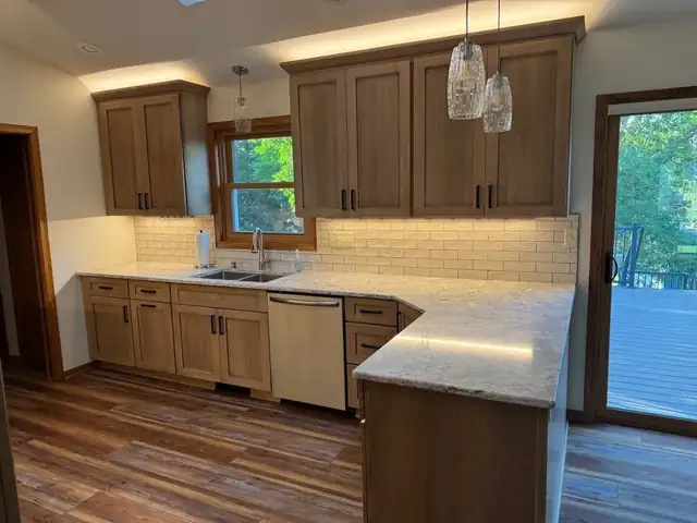 Kitchen remodel with warm wood cabinets, under-cabinet lighting, glass pendants and granite peninsula next to a patio door