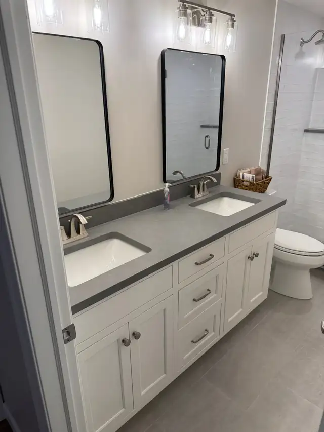 Double vanity bathroom with white cabinets, gray counter, black framed mirrors and matte black faucets