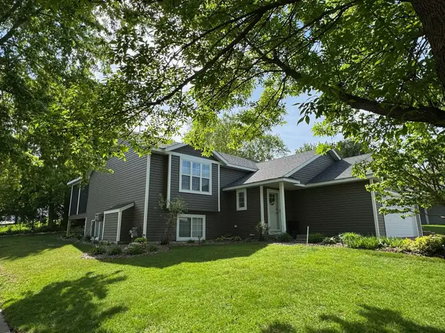 Front exterior of a split-level home with gray siding, new windows and a shaded front lawn