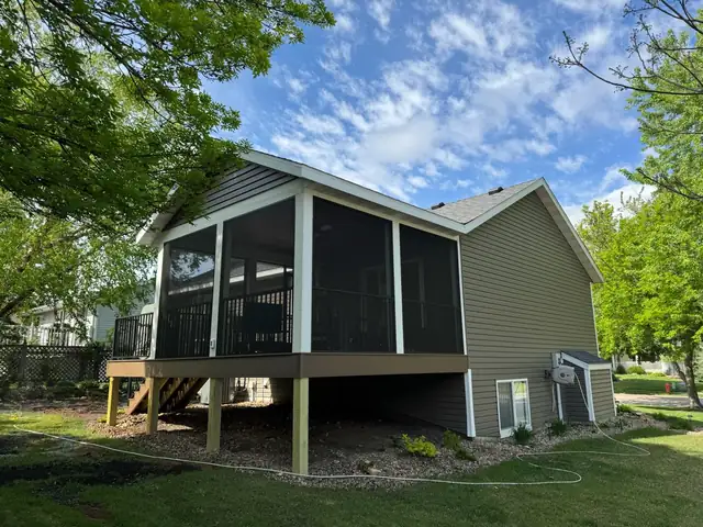 Screened porch addition built on posts off the back of a two-story home with green siding