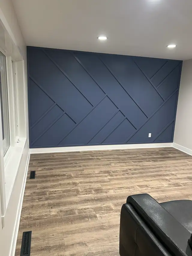 Finished basement room with navy accent wall and diagonal trim pattern, recessed lights and wood-look vinyl plank floor