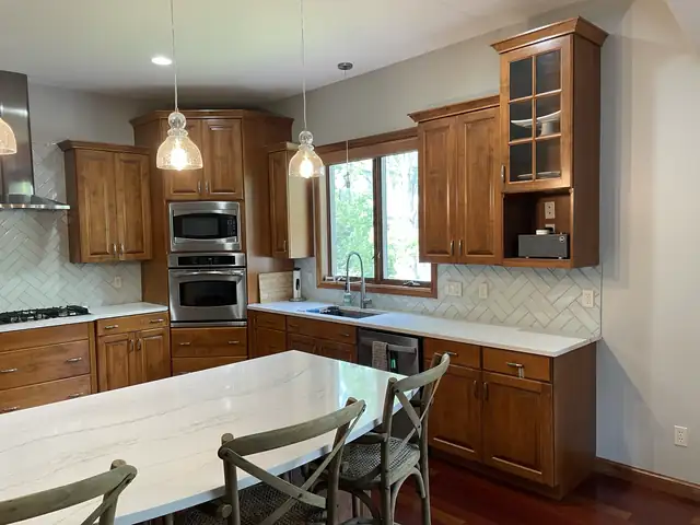 Kitchen remodel by Goldsmith Remodel and Design with cherry cabinets, a white quartz island, glass pendants and a stainless range hood