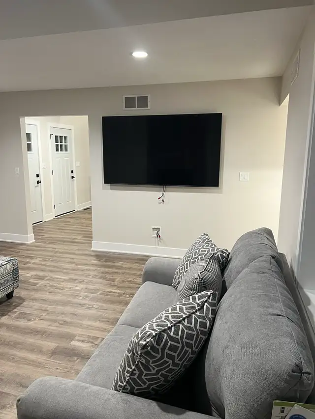 Finished basement family room with wall-mounted TV, sectional sofa and wood-look plank floor