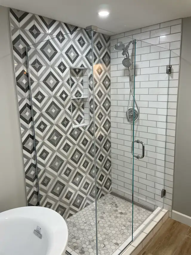 Glass shower with black and white geometric tile accent wall, white subway tile and pebble floor